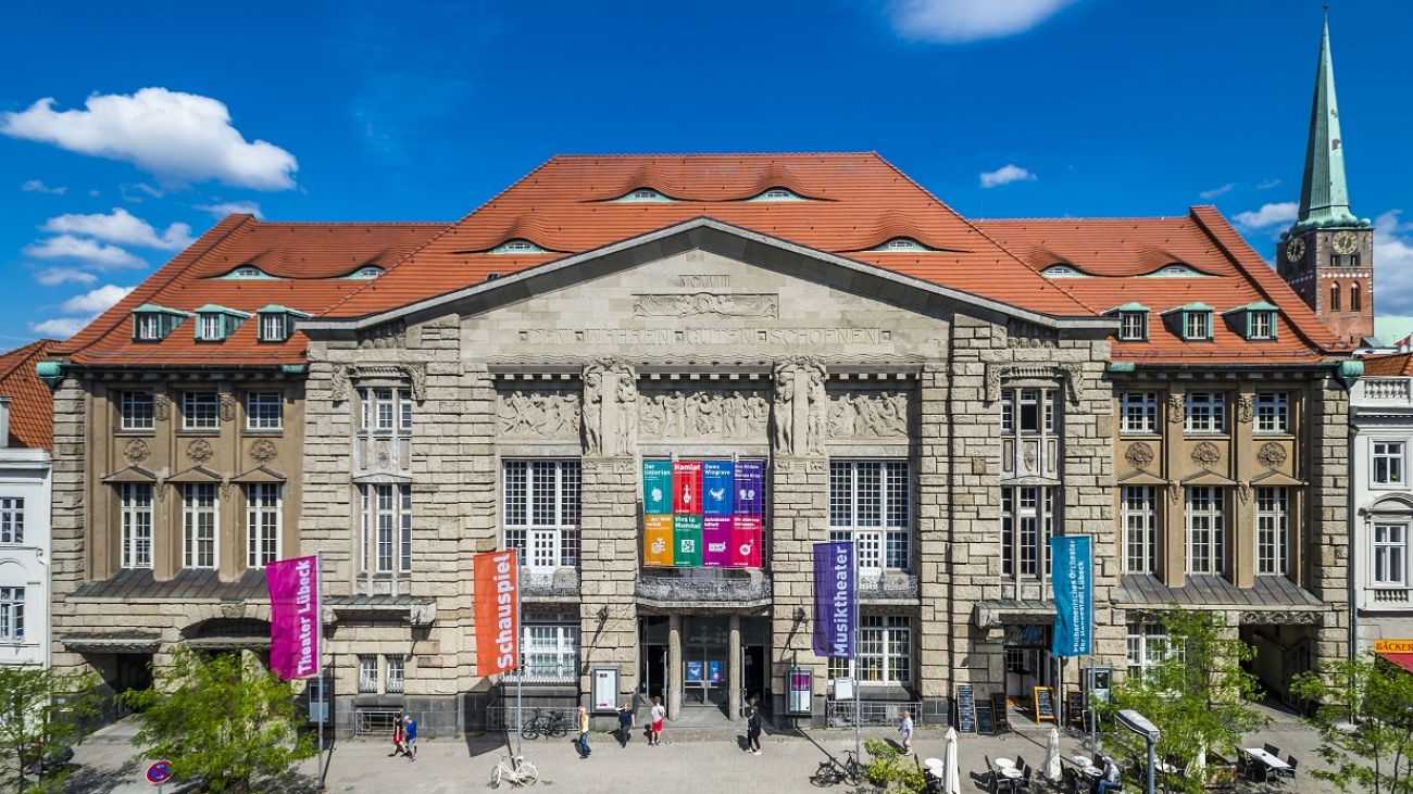 Frontansicht des Theaters Lübeck: Ein graues dreistöckiges Gebäude mit zwei Säulen und Tympanon