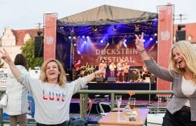 Zwei feiernde Frauen vor einer Bühne, auf der "Duckstein-Festival" steht