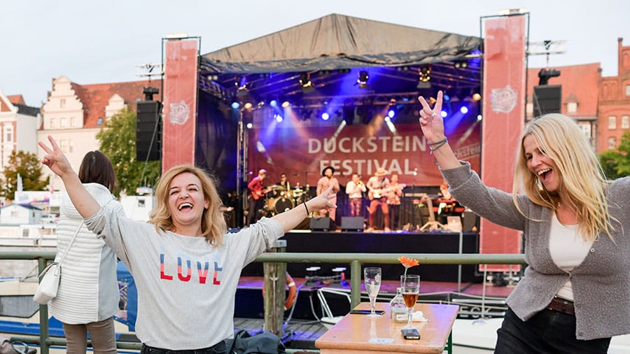 Zwei feiernde Frauen vor einer Bühne, auf der "Duckstein-Festival" steht