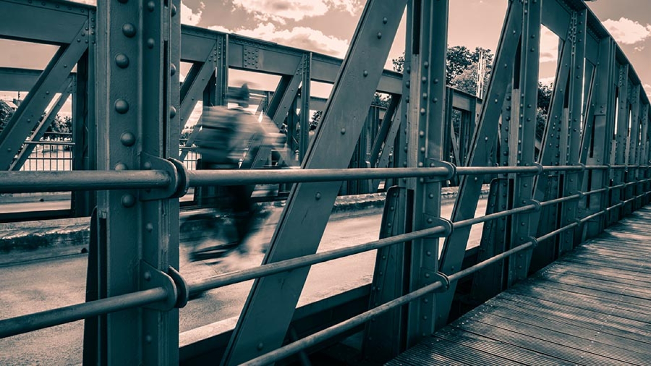 Durch die Stahlstreben der Drehbrücke sieht man einen Fahrradfahrer mit starker Bewegungsunschärfe
