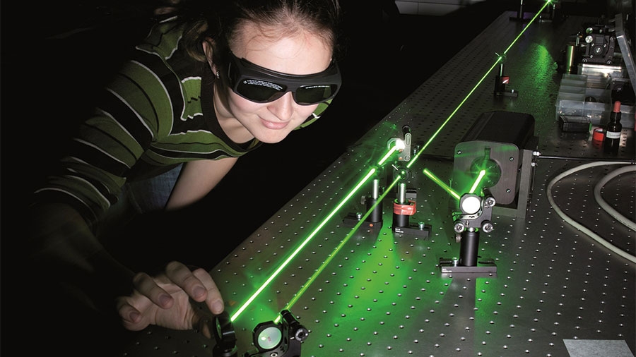 Eine Studentin arbeitet mit einem grünen Laser in einem dunklen Raum und trägt eine Schutzbrille.