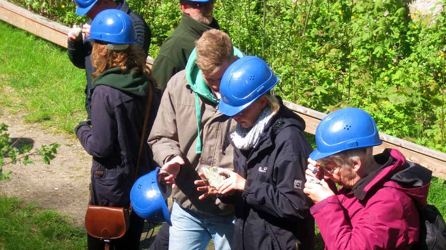 Eine Gruppe Menschen mit blauen Helmen begutachten Gestein, das sie in den Händen halten
