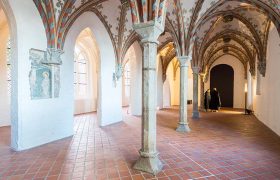 Ein Blick in das Burgkloster im Europäischen Hansemuseum: Weiße Wände mit gotischem Gewölbe und Backstein-Fußboden