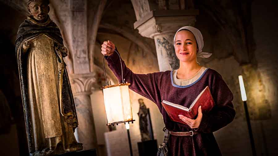Eine junge Frau in mittelalterlicher Kleidung hält eine Laterne in die Höhe