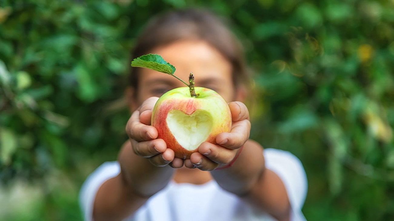 Ein Mädchen hält einen Apfel mit einem eingeschnitzen Herz hoch.