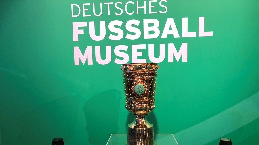 Vor einer grünen Wand mit der Aufschrift "Deutsches Fussball Museum" steht der DFB-Pokal