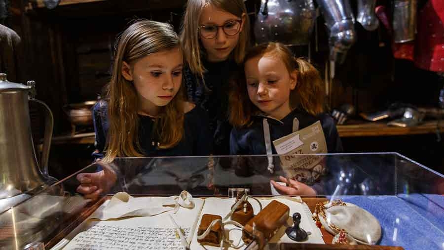 Drei Kinder betrachten in einer Museumsumgebung einen Schaukasten mit einer Urkunde