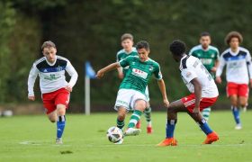 Mehrere Spieler des VfB Lübeck in grün-weißer Spielkleidung kämpfen gegen Spieler des HSV in blau-weißen Trikots und roten Hosen