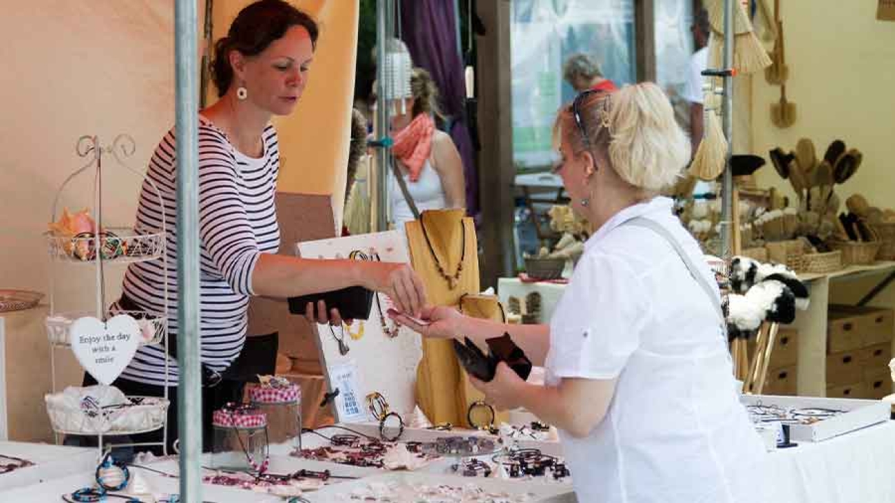 Auf einem Markt bezahlt eine Kundin an einem Stand mit Ketten und Ringen