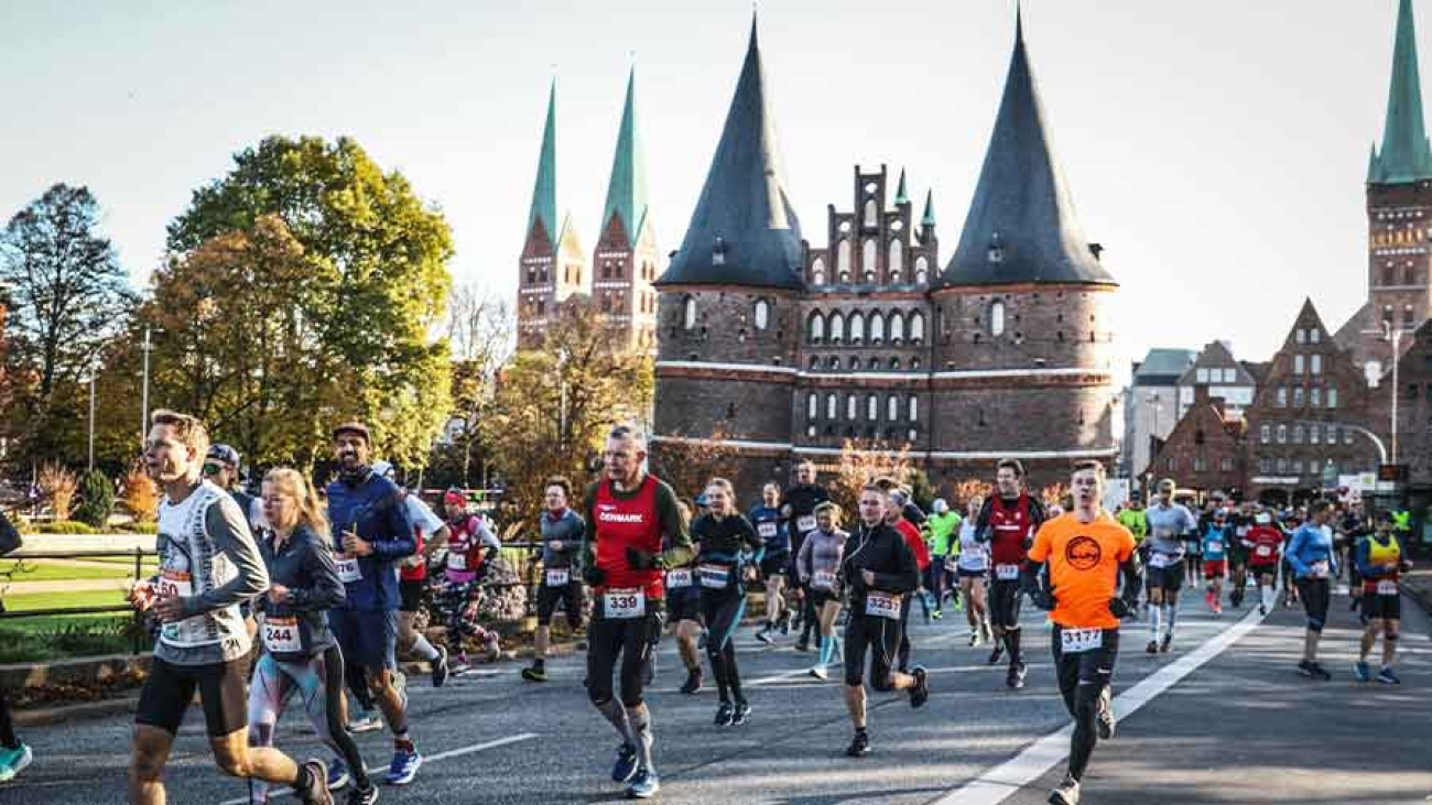 Vor dem Holstentor laufen viele Menschen in Sportkleidung und mit Startnummern