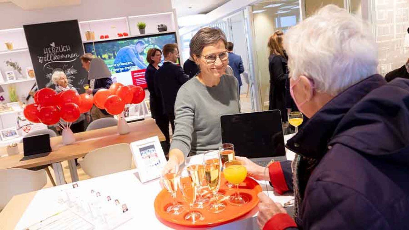 Zwei Frauen sind an einem Beratungstresen im Gespräch. Das Ambiente ist eine Eröffnungsfeier