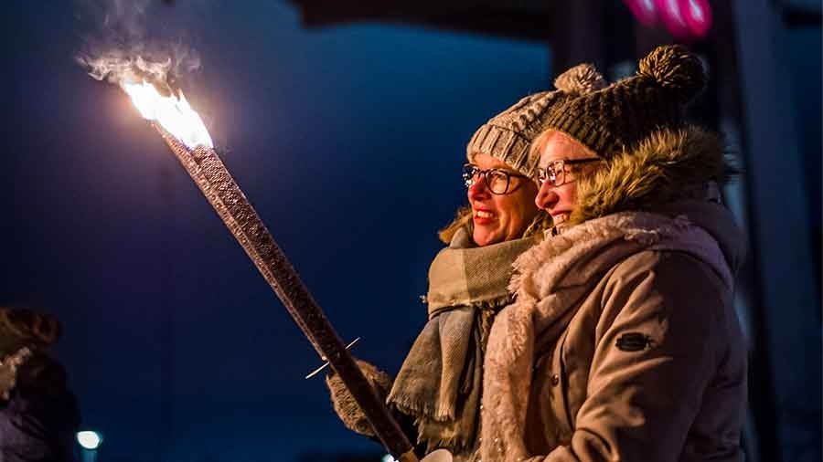 Zwei Frauen in Winterkleidung halten Fackeln hoch und schauen in die Flammen