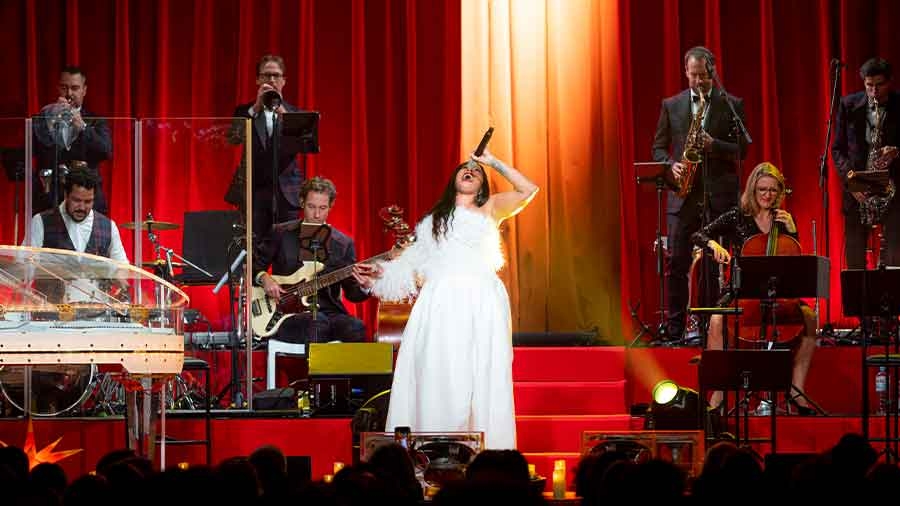 Vor einer Bühne mit Jazz-Orchester singt eine Frau in weißem Kleid sehr enthusiastisch