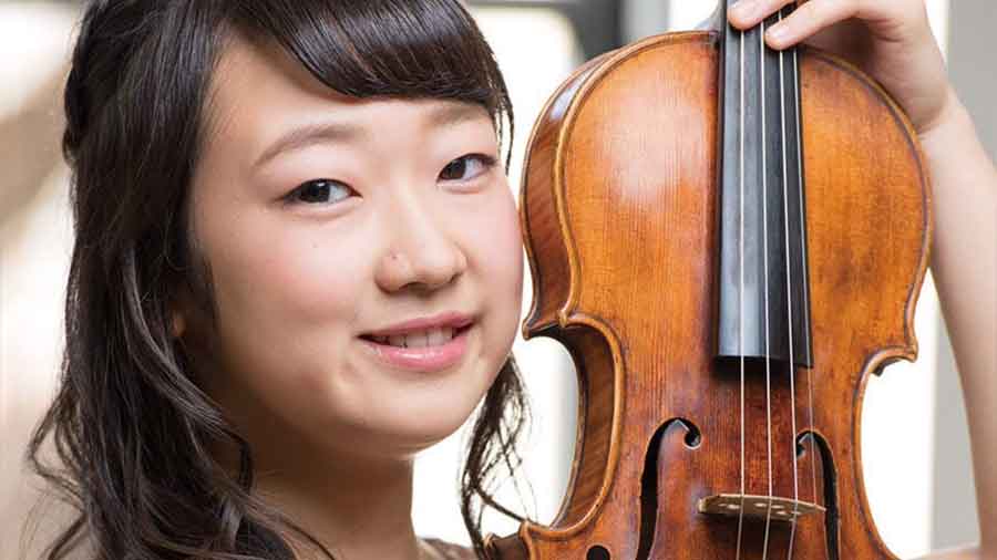 Eine junge Frau mit schwarzen Haaren hält lächelnd eine Violine neben ihr Gesicht