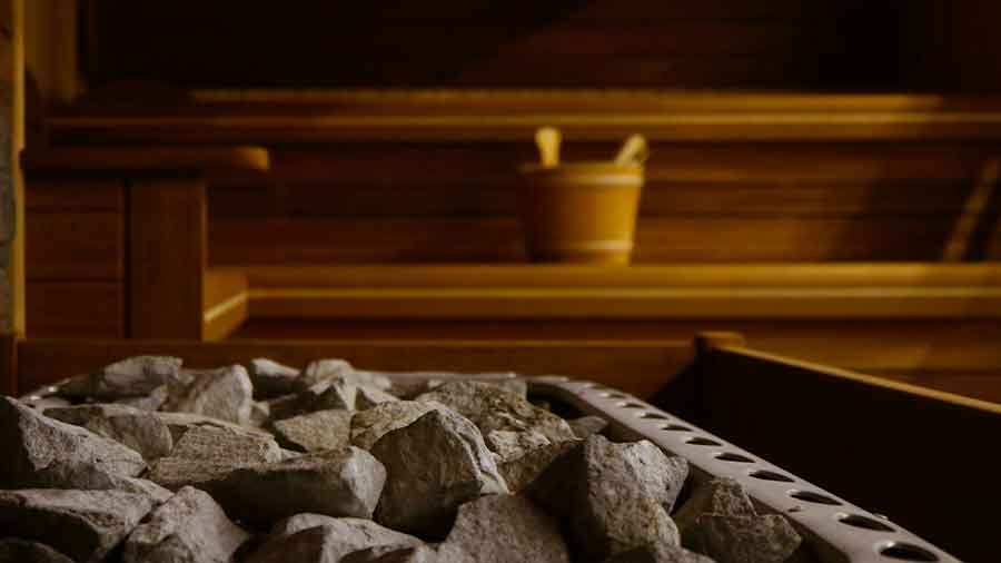 Das Innere einer Sauna: Man sieht im Vordergrund Steine, im Hintergrund eine Holzbank mit Holzeimer