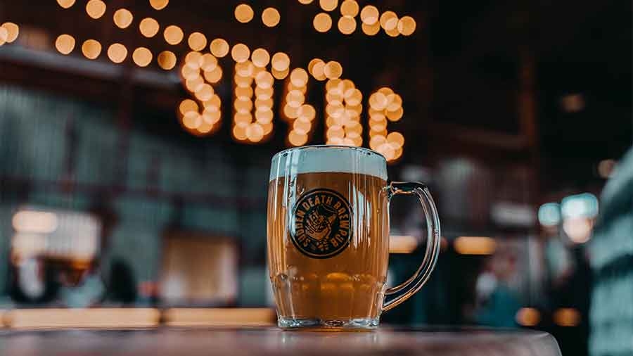 Ein Glas Bier mit dem Aufdruck "Sudden Death" steht vor der Beleuchtung SD/BC