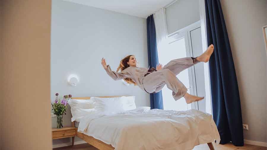 Eine junge Frau in Pyjama springt rückwärts auf ein Bett in einem Hotelzimmer