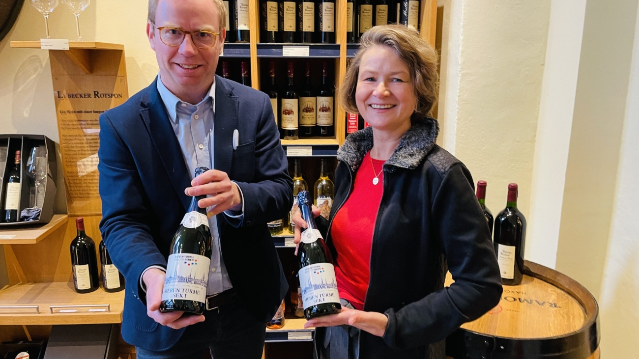 Ein Mann und eine Frau halten jeweils eine Flasche Sekt in die Kamera