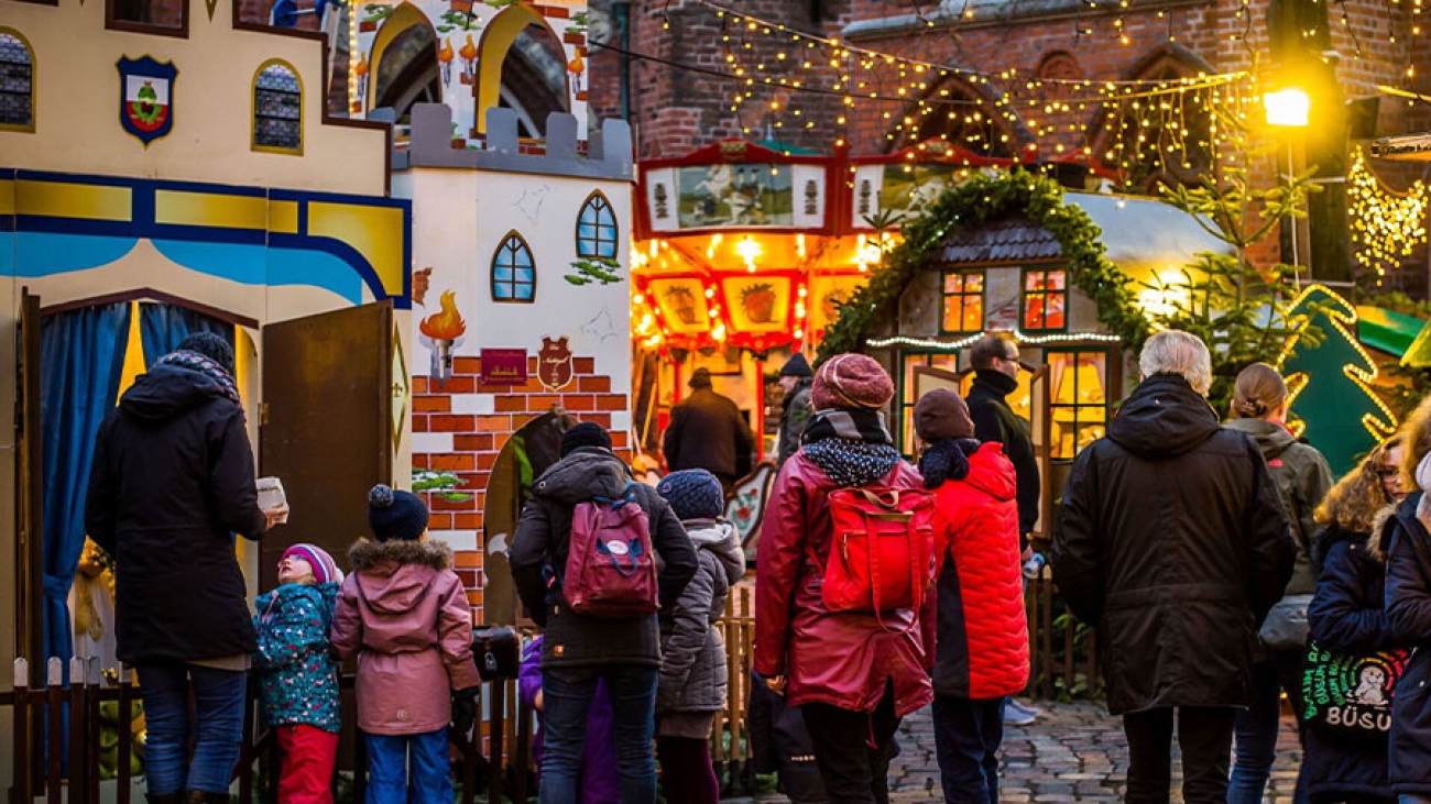 Auf einem Weihnachtsmarkt sind mehrere Erwachsene und Kinder zu sehen