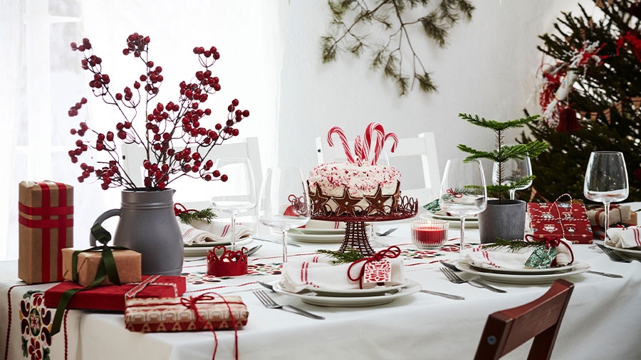 Auf einem festlich geschmückten Tisch steht eine Torte, mehrere Geschenke und ein Strauß mit roten Beeren. Insgesamt ist das Bild sehr hell, rot und weiß dominieren