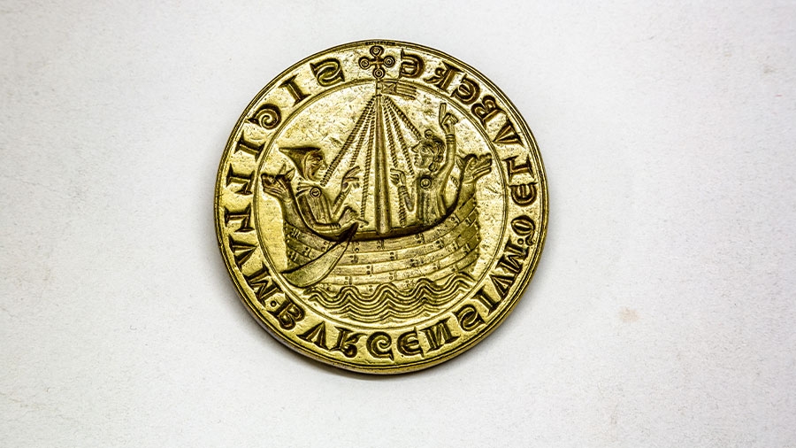 Ein goldenes Stadtsiegel der Hansestadt Lübeck mit einem Boot und zwei Personen drauf.