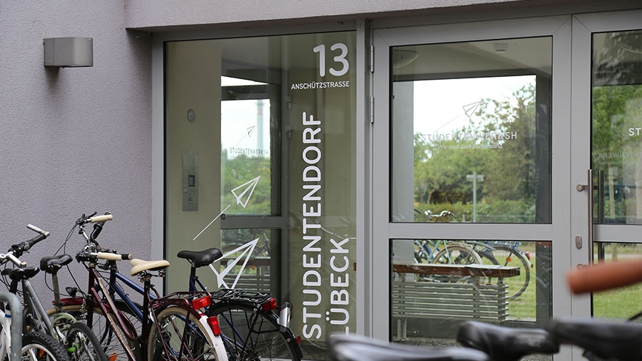 Eingangssituation einer Wohnanlage. Im Vordergrund viele Fahrräder. An der Tür steht groß "Studentendorf Lübeck"