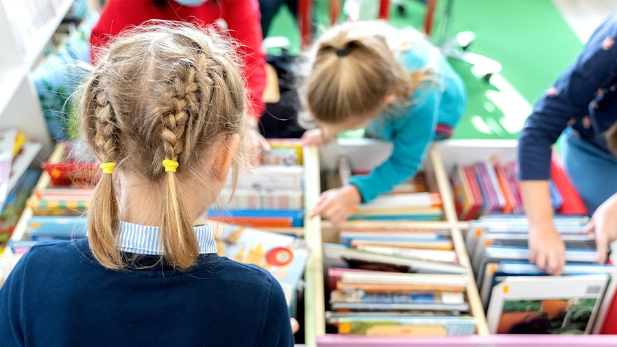 Ein Mädchen mit Zöpfen sucht nach einem Kinderbuch im Regal.