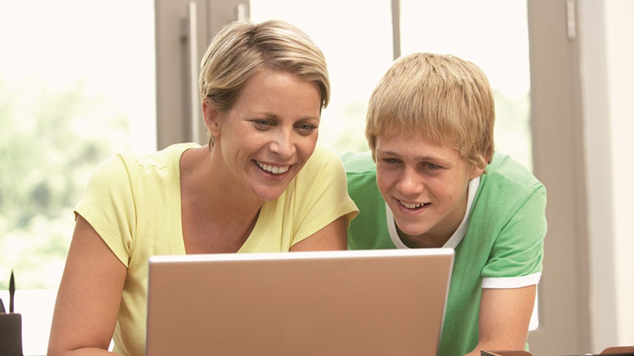 Eine Mutter und ihr Sohn schauen auf einen Laptop und freuen sich.