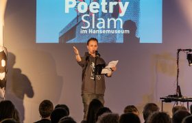Ein junger Mann steht bei einer Poetry Slam Veranstaltung im Hansemuseum auf der Bühne.