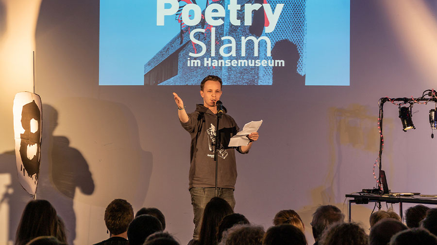 Ein junger Mann steht bei einer Poetry Slam Veranstaltung im Hansemuseum auf der Bühne.