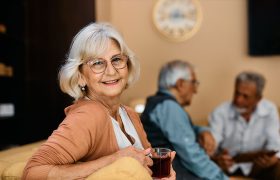Eine ältere Frau mit einer Tasse Tee in der Hand lächelt in die Kamera.