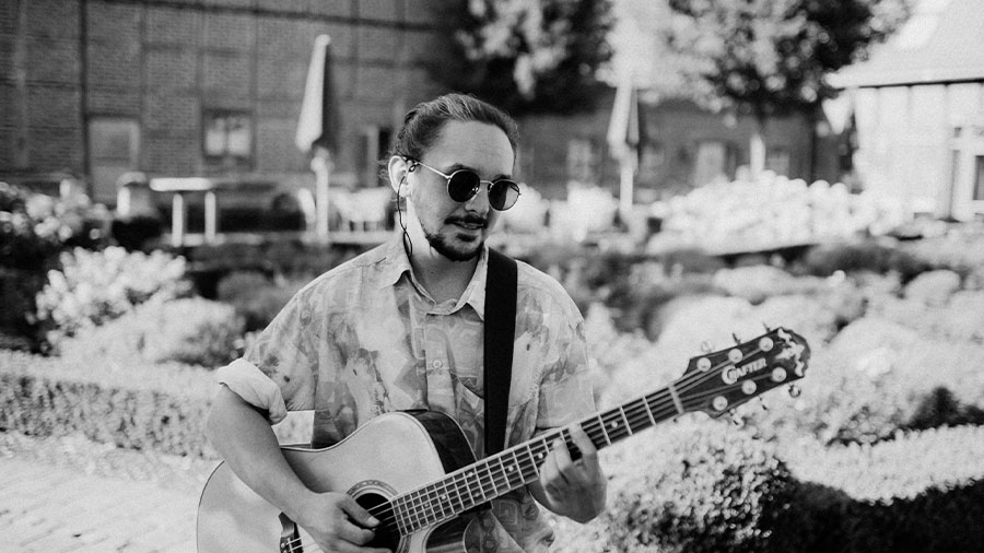 Der Künstler Parula hat eine Gitarre in der Hand und eine Sonnenbrille auf in einem schwarz weiß Bild.