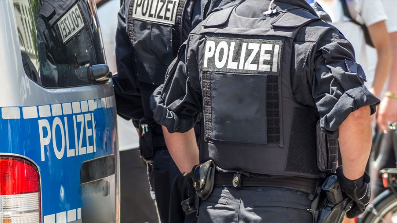 Zwei Polizisten stehen neben ihrem Polizeiauto mit dem Rücken zur Kamera.