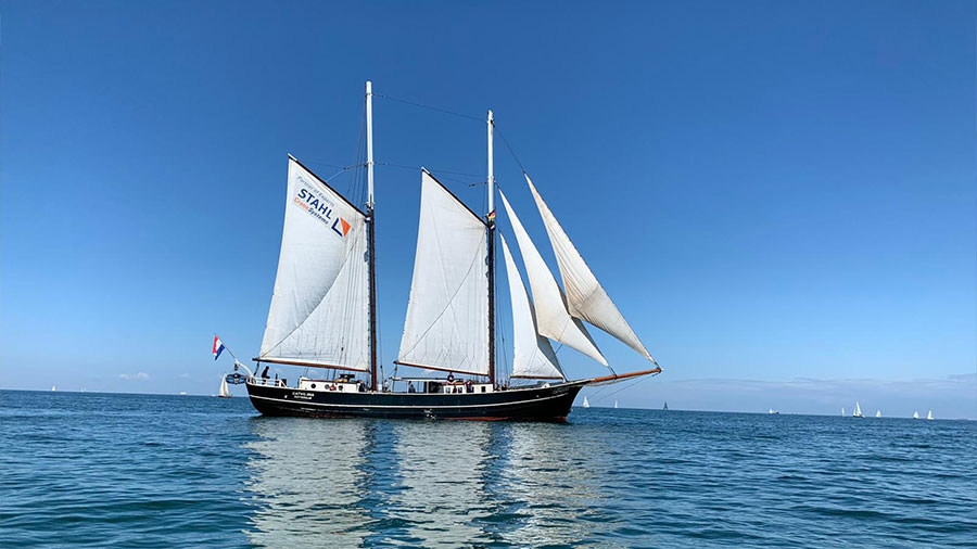 Ein Segelschiff mit zwei Masten fährt auf offener See unter Niederländischer Flagge.