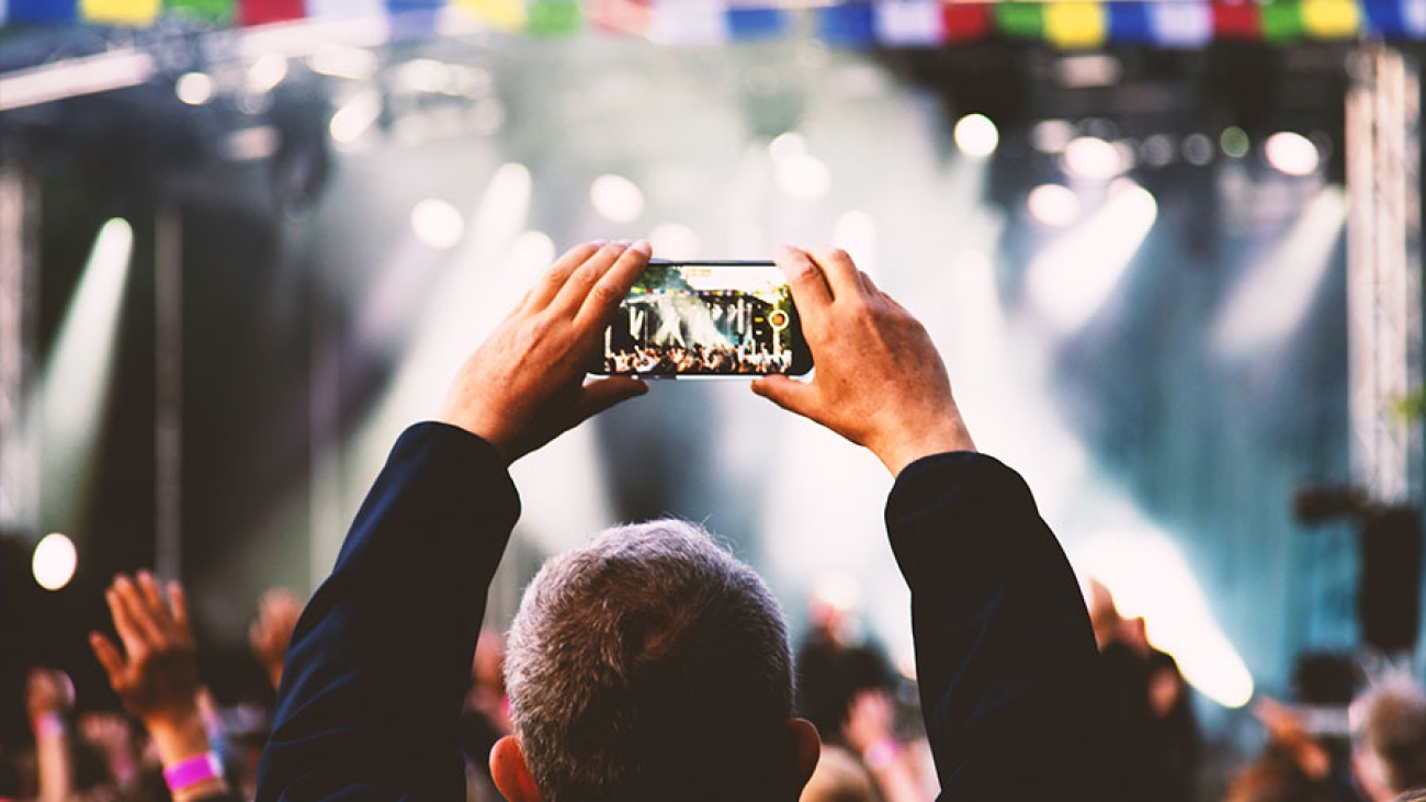 Ein Mann hält sein Handy hoch, um die Bühne auf einem Festival zu filmen.