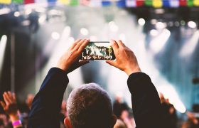 Ein Mann hält sein Handy hoch, um die Bühne auf einem Festival zu filmen.