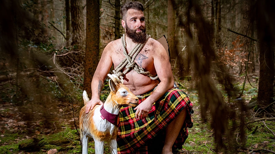 Ein Mann ist Wikingerkleidung hockt neben der Ziege im Wald.