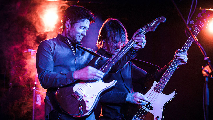 Zwei Männer spielen auf einer bunt beleuchteten Bühne Gitarre.