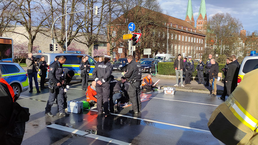 Aktivisten kleben auf der Straße und die Polizei versucht sie zu lösen.