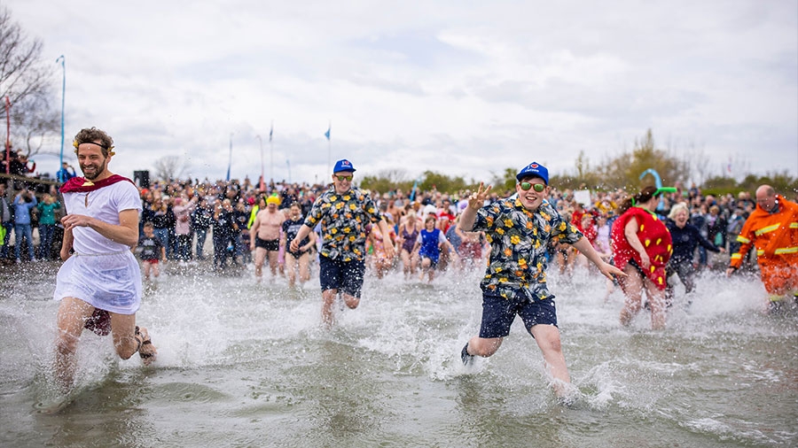 Mehrere Menschen mit Kostümen rennen ins kalte Wasser der Ostsee.
