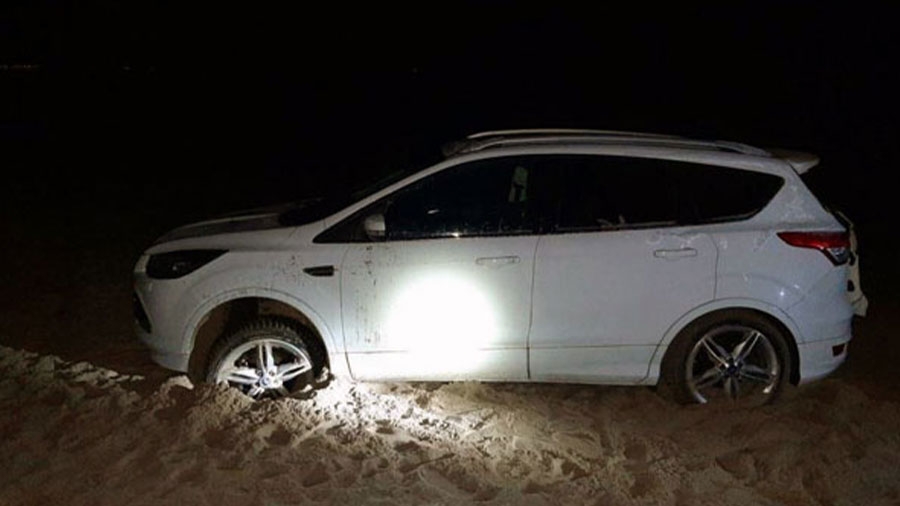 Ein weißes Auto steckt im Sand fest.