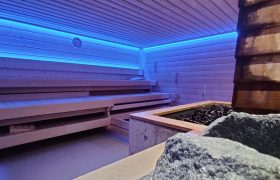 Eine Sauna, die im Licht von blauen LED Leuchten erscheint, mit Saunasteinen und allem was dazu gehört.