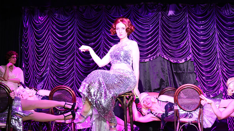 Eine Frau mit Glitzerkleid sitzt auf einem Stuhl in lila Licht.