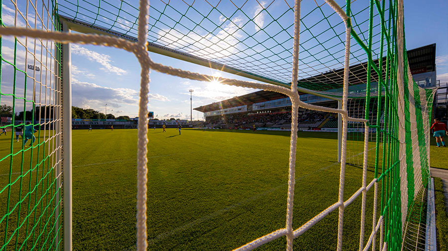 Ein Fußballfeld in der Sonne wird durch das Tornetz fotografiert.