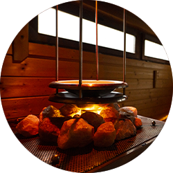 Über einem Feuer mit Steinen in der Sauna hängt ein Topf.