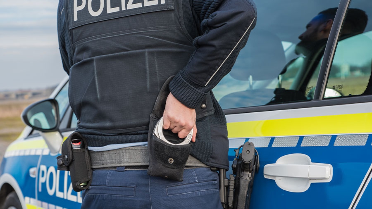 Ein Polizist greift seine Handschellen, während er scheinbar die Tür eines Polizeiautos auf macht.