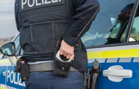 Ein Polizist greift seine Handschellen, während er scheinbar die Tür eines Polizeiautos auf macht.