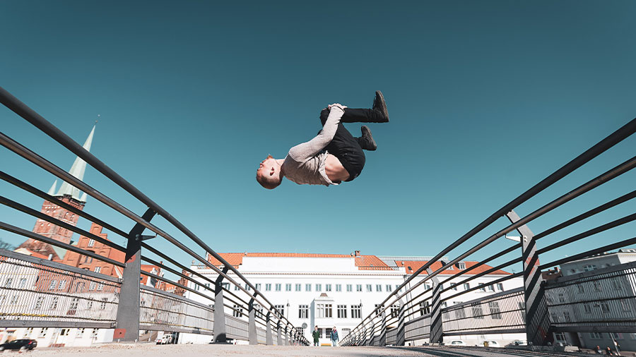 Ein junger Mann macht einen Salto auf einer Brücke.