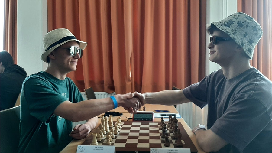 Zwei Schachspieler sitzen sich gegenüber und geben sich die Hand.