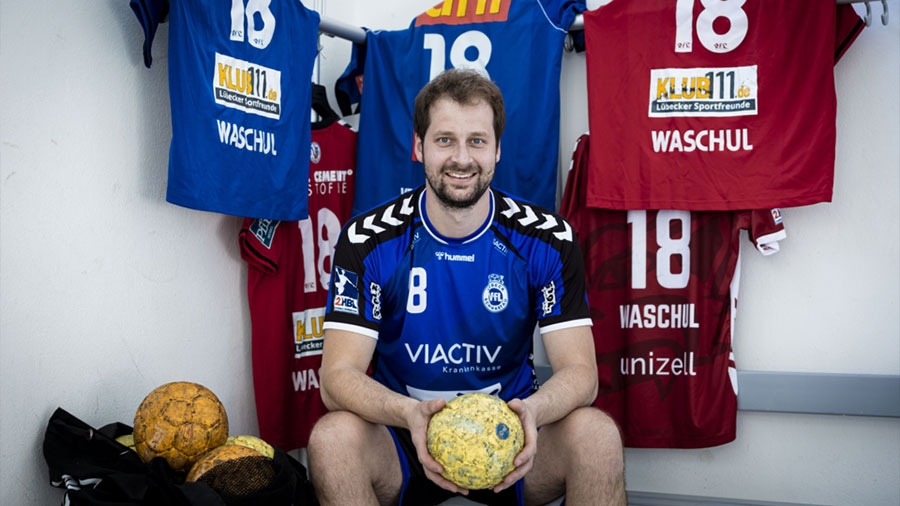 Ein Spieler des VfL sitzt in der Kabine vor Trikots mit einem Ball in der Hand.